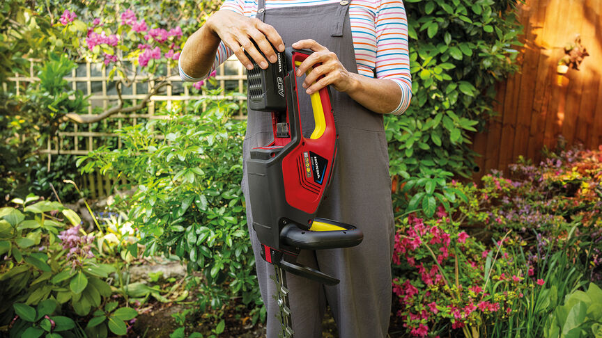 Mujer que utiliza un cortasetos a batería Honda para cortar un seto en un jardín.