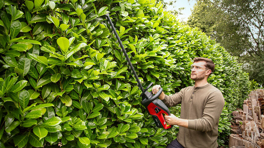 Mujer que utiliza un cortasetos a batería Honda para cortar un seto en un jardín.