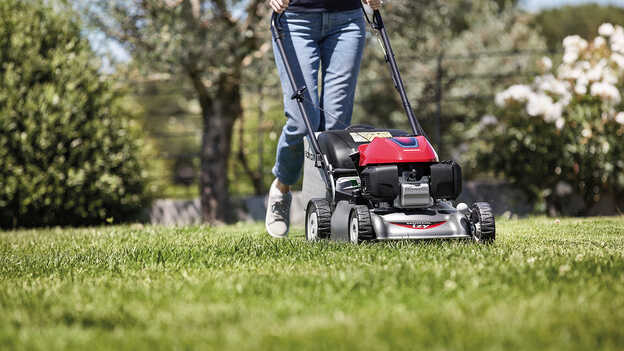 Side view of Honda IZY lawnmower with a woman in the garden